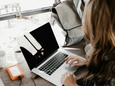 girl wearing grey long-sleeved shirt using MacBook Pro on brown wooden table